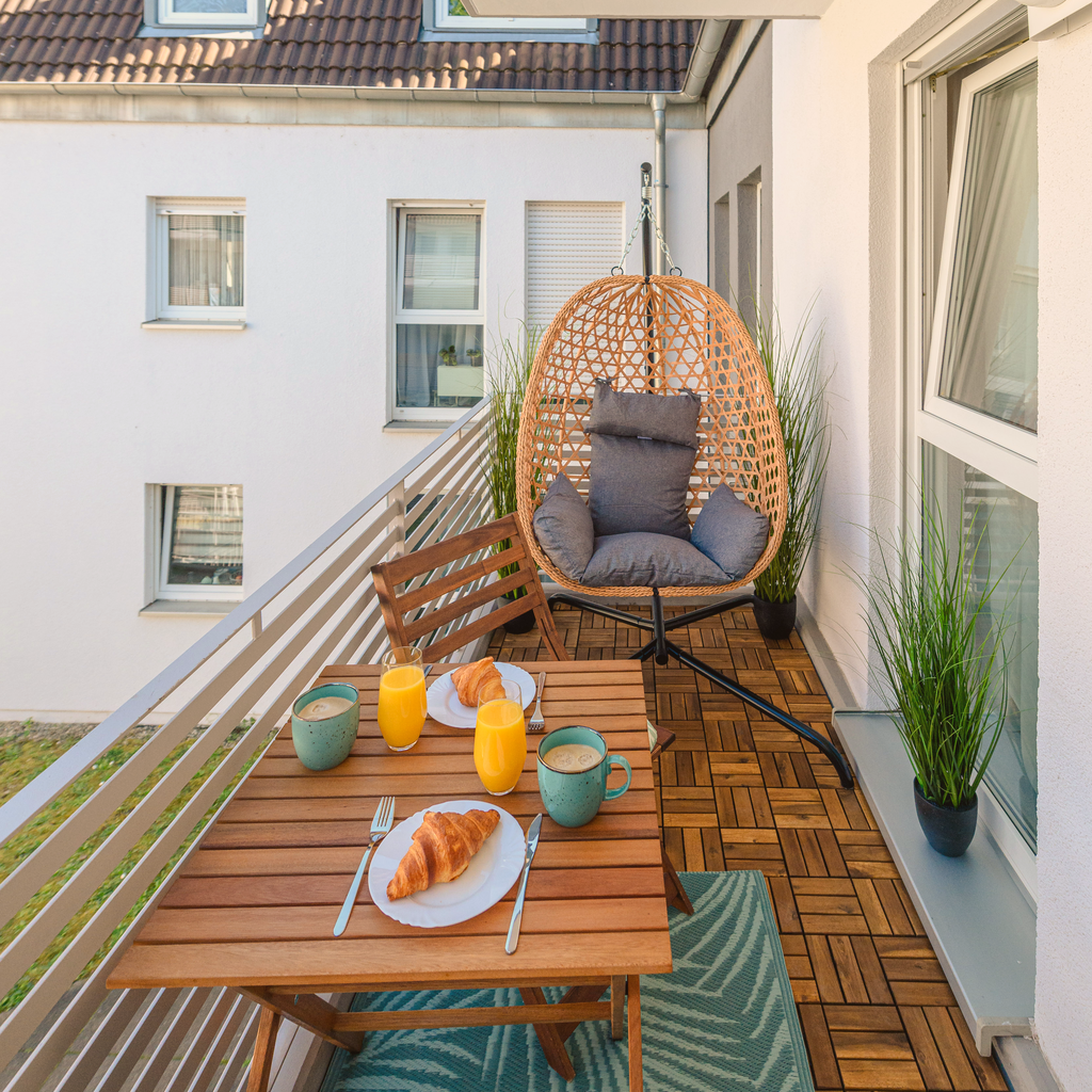 Sonniger Balkon der Ferienwohnung Maxi II mit gedecktem Frühstückstisch, Hängesessel und Grünpflanzen